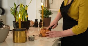 Woman in black apron cutting traditional Easter pastry with knife and tasting it at kitchen with daffodils and Easter holiday home decoration with candles. High quality 4k video footage