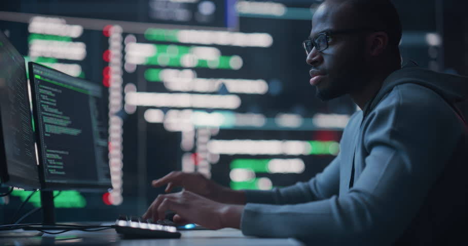 Dolly Shot of a Black Male Programmer Working in a Monitoring Control Room, Surrounded by Big Screens Displaying Lines of Programming Language Code. Portrait of a Man Creating a Software and Coding | Shutterstock HD Video #1100883685