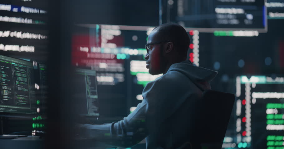 Dolly Shot of a Black Male Programmer Working in a Monitoring Control Room, Surrounded by Big Screens Displaying Lines of Programming Language Code. Portrait of a Man Creating a Software and Coding | Shutterstock HD Video #1100883689
