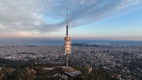 Collserola antenna tower at sunset on Tibidabo with Barcelona city in background, Spain. Aerial circling