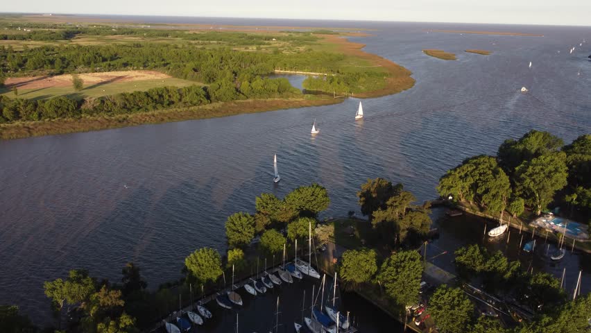 Sailboats navigating along maritime route between Buenos Aires in Argentina and Montevideo in Uruguay, San Isidro Yacht club along Rio de la Plata river at sunset. Aerial drone panoramic view 