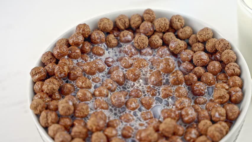 Chocolate cereal with white dairy foam in a white bowl. Cereal with milk for breakfast. Close-up. Slow motion.