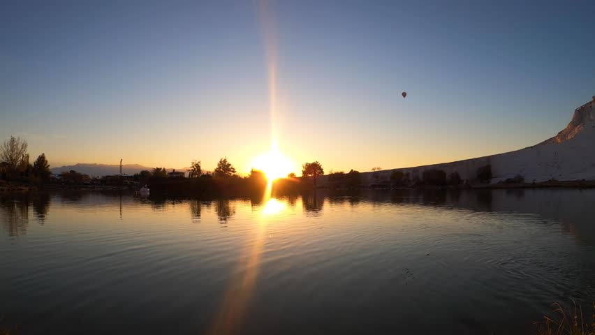 time lapse of a sunset reflecting in the lake with hot air ballon in flying over the sky - Pamukalle, Turkey