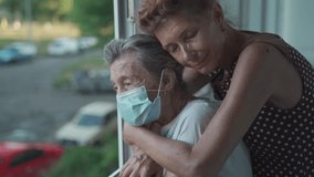 Adult daughter embracing with loving senior mother 90 years in mask standing at window, relatives from different generations, women standing in embrace, dreaming of happiness, spending time together. - Powered by Shutterstock - Get 15% off with code: PIKWIZARD15