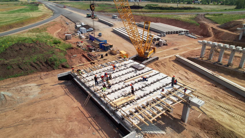 Construction team in hard hats work at the construction site aerial view. Concrete structure. Builders in the process of work. Construction Crane. Construction of a road bridge | Shutterstock HD Video #1100892471
