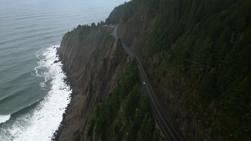 Drone cinematic aerial dramatic shot of Coastline Road, Cannon beach, Oregon. Green forest mountains, hills. Cloudy mist weather. Pacific coast highway. Cars on highway road. High quality 4k footage Royalty-Free Stock Footage #1100892921
