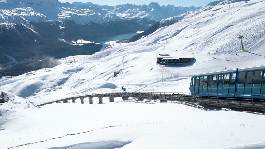 Blue cable car going down surrounded by snowy winter landscape and mountains in St. Moritz, Switzerland.