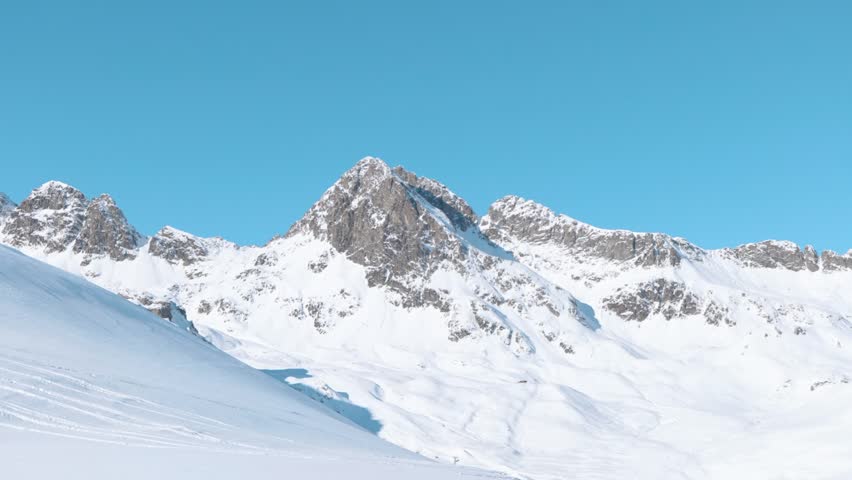 Caucasian man walks through winter landscape and stops to take pictures with his camera of snow covered mountain peaks.