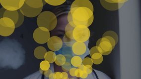 Animation of yellow dots over caucasian female doctor in face mask. Medicine, health and pandemic concept digitally generated video.