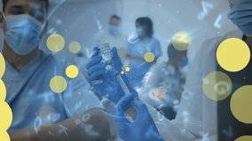 Animation of yellow dots over caucasian male doctor in face mask with vaccine. Medicine, health and pandemic concept digitally generated video.