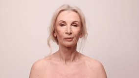 Beautiful middle-aged woman applying clay face mask. Model posing over grey studio background. Natural ingredients. Concept of natural beauty, face skin care, cosmetology and cosmetics, health