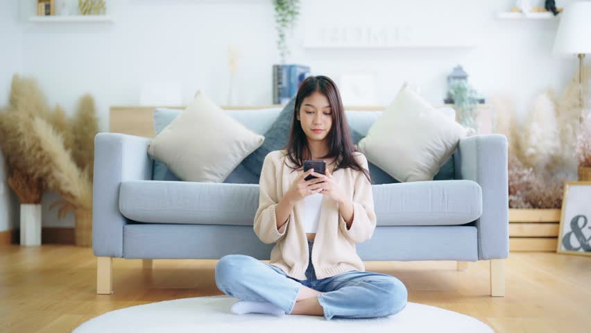 Happy young asian woman relax on comfortable couch at home texting messaging on smartphone, smiling girl use cellphone, chatting online message, shopping online from home | Shutterstock HD Video #1100902061