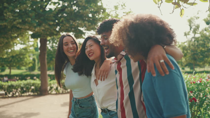 Happy multiethnic young people walk embracing on summer day outdoors. Group of friends are talking and laughing merrily while walking along path in city park Royalty-Free Stock Footage #1100905127