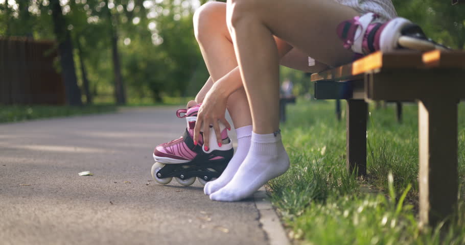 Woman sitting on park bench puts on rollerblades