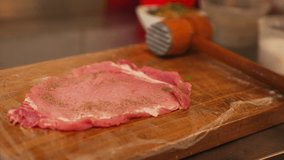 Chef seasons raw pork cutlet chop on wooden board for preparing Schabowy Kotlet. Polish traditional cuisine. High quality 4k footage