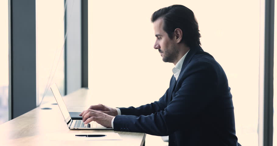 Young businessman sit in contemporary office, typing on laptop. Serious financial analyst work with online data, draws a contract, prepares report, chatting and messaging online. Business technology | Shutterstock HD Video #1100909957