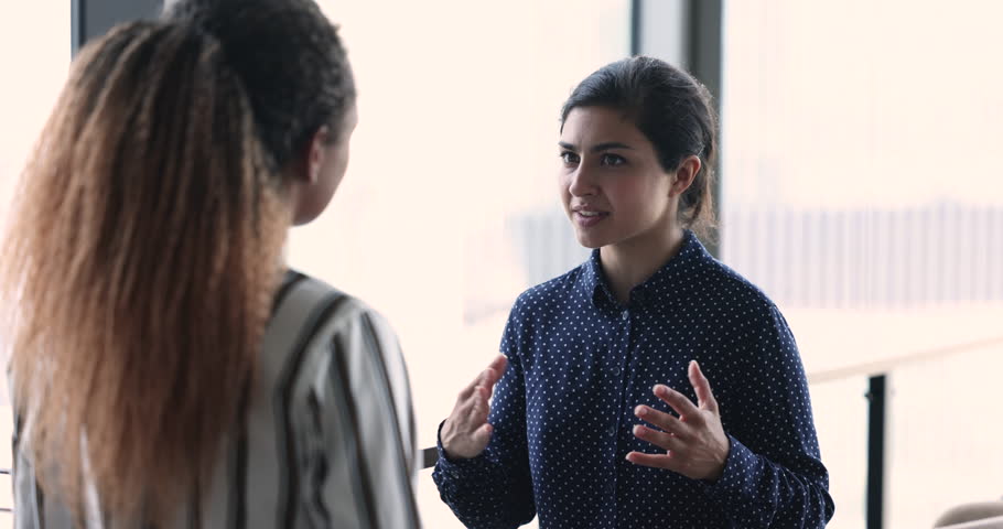 Young Indian business woman share thoughts, explain issue, search solution, thinking, provide information during meeting with African colleague. Advisory, consultation, teamwork of workmates in office | Shutterstock HD Video #1100910067