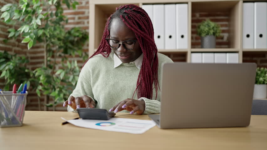 African woman with braided hair working using laptop and calculator at office | Shutterstock HD Video #1100911611
