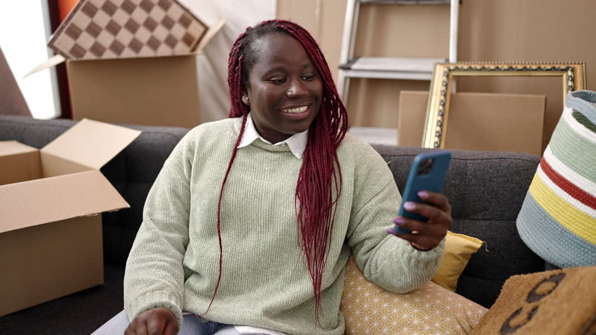 African woman with braided hair doing video call sitting on the sofa at new home