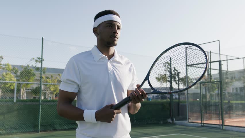 Athletic young black man in headband hitting ball with tennis racquet while playing at sports court Royalty-Free Stock Footage #1100913861