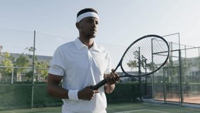 Athletic young black man in headband hitting ball with tennis racquet while playing at sports court