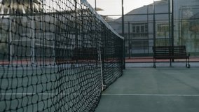 Young biracial man picking up tennis ball by net during tennis practice at sports court
