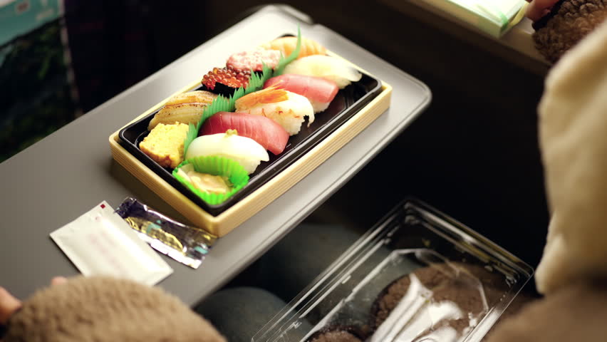 4K Asian woman eating traditional Japanese food sushi and egg roll in lunch box bento during travel on train. Attractive girl travel on railroad transportation on winter holiday vacation.
