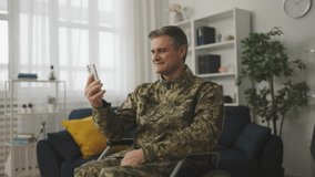 Smiling man wheelchair user in military uniform having video call with relatives
