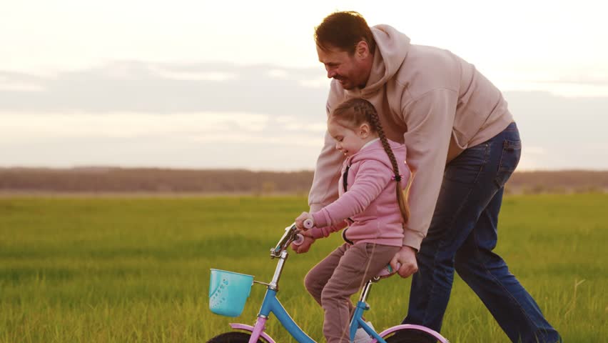 father rides child two-wheeled bicycle sunset. happy family. happy child concept. child dream bike. child rides bicycle sun green field grass. daughter girl dad nature park riding children bike. Royalty-Free Stock Footage #1100921367