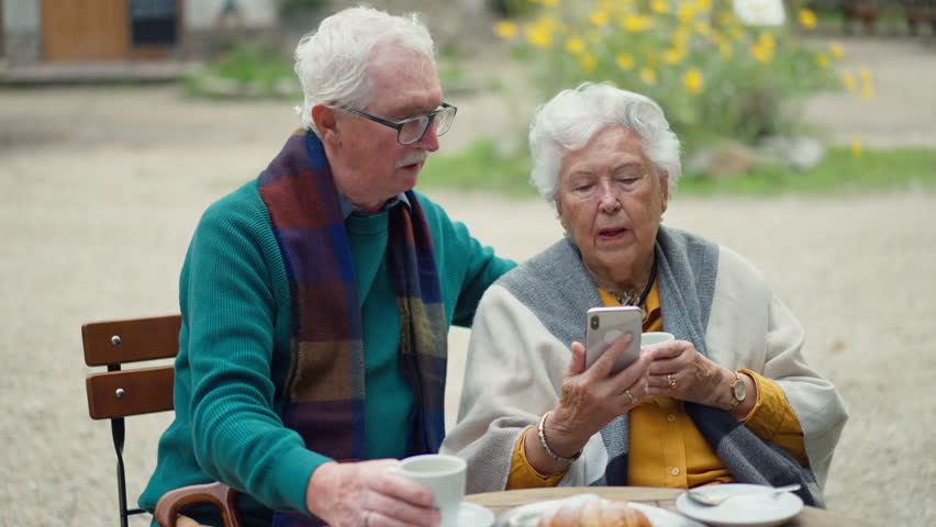 Happy senior couple in forest buffet resting after walk, having beer and looking at smartphone.