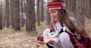 Bulgarian girl in traditional folklore costume  in forest hold in hands pine cones, Rhodopes mountain, 4k slow motion video. Bulgaria nature