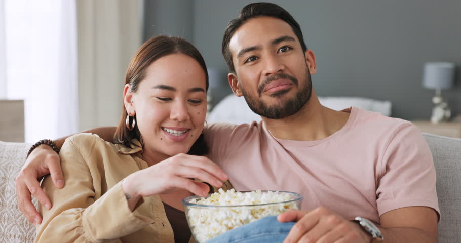 Couple in living room, eating popcorn and tv streaming comedy movie on home sofa together. Happy young love marriage, asian woman leisure time snack on couch and latino man smile watch youtube video Royalty-Free Stock Footage #1100930251