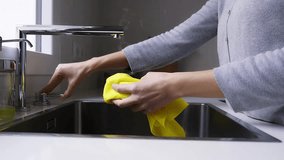 4k video of unrecognizable woman wiping clean sink and faucet with wet yellow cleaning cloth. Squeezing cloth.