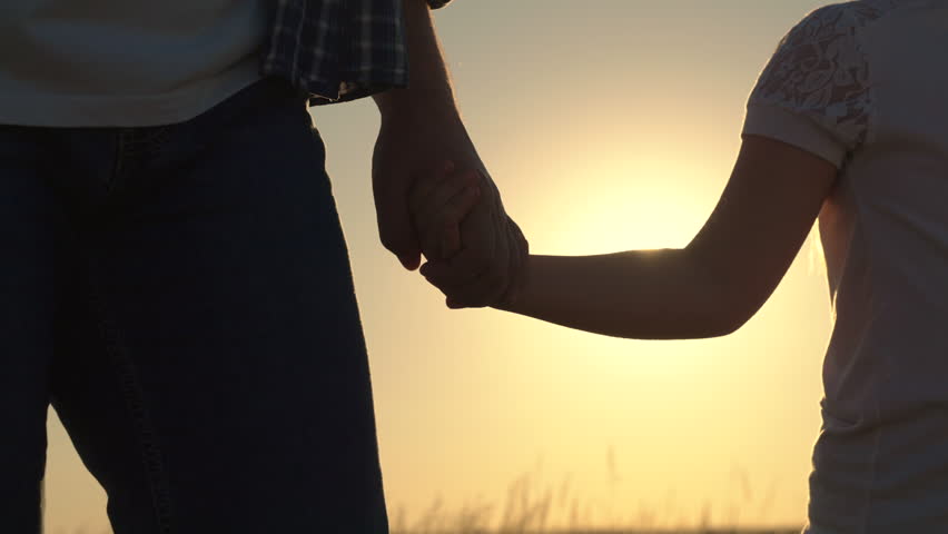 Happy family. Little daughter, dad are walking holding hands in park against sun. Father walks with child in summer at sunset, concept of family trust. Parent, girl is walking. Girl, dad hand in hand