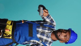 Vertical video: African american man painting walls with brush in studio, using renovating tools to change color. Professional builder working with paintbrush on carpentry equipment over blue backdrop - Powered by Shutterstock - Get 15% off with code: PIKWIZARD15