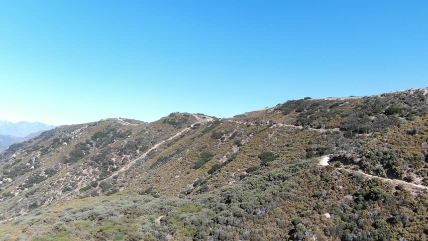 Aerial of dirt road in Big Bear high desert green mountains against blue sky