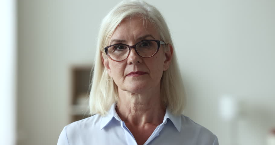 Happy mature businesswoman in casual blouse, head shot. Professional occupation person, businesslady portrait. Blond woman in glasses pose standing alone indoor smile looking at camera, close up face Royalty-Free Stock Footage #1100936499