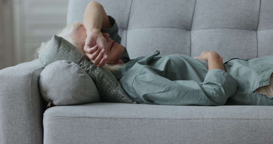 Close up weak or sick aged woman lying down on sofa at home looks exhausted or depressed, relieving fatigue, rest on couch in living room, having migraine, headache or sleep disorder, having day nap Royalty-Free Stock Footage #1100936513