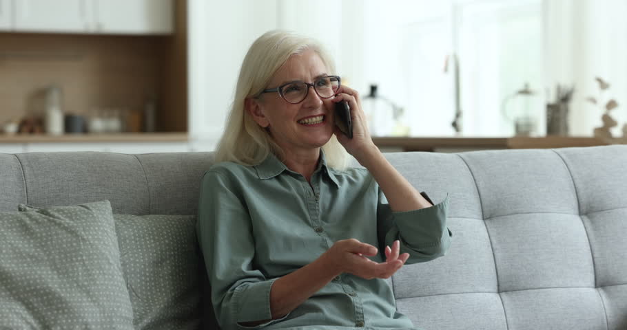 Attractive woman pensioner talk on mobile phone at home, rest on cozy sofa in living room, has good conversation with friends, relatives, happy to share news. Spend carefree time use modern technology Royalty-Free Stock Footage #1100936565