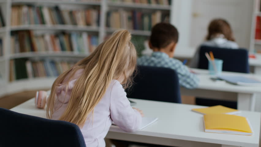 Back view shot of group of little kids studying at classroom, cute schoolgirl turning to camera and smiling, tracking shot, slow motion, empty space Royalty-Free Stock Footage #1100938341