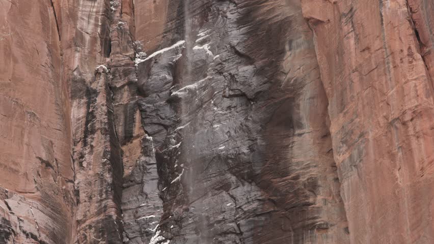 The waterfall at the Temple of Sinawava in Zion Nat. park Utah, USA has just enough water coming down to create a fine ethereal mist that cascades down the red sandstone cliff past snow laced ridges.