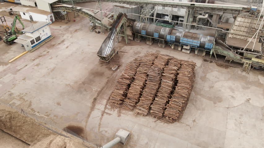 Backward shot of drone flying above huge sawmill. Trunks stacked together and big pile of sawdust 