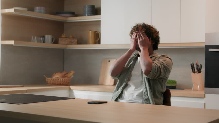 Worried nervous Indian man stress sitting at home kitchen rubbing eyes feel despair lost receive bad news in phone message. Stressed anxious Arabian guy male feeling upset thinking of business problem Royalty-Free Stock Footage #1100943593