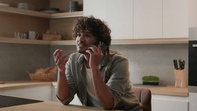 Moving shot laughing smiling cheerful Indian man talking phone in home kitchen. Happy Hispanic guy talk with friends by smartphone Arabian male homeowner speak mobile friendly business conversation - Powered by Shutterstock - Get 15% off with code: PIKWIZARD15