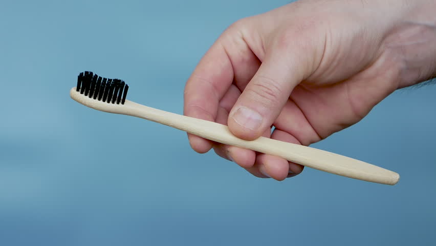Lose-up of a wooden toothbrush in a person's hand on a blue background. Eco toothbrush. | Shutterstock HD Video #1100945315