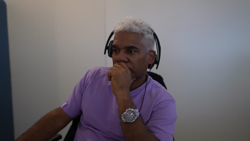 Solid businessman with gray hair sits in a meeting in a modern office, watches a mobile app