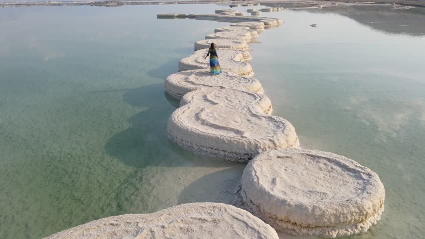 Aerial Shot Of Woman Walking On Salt Formation At Dead Sea During Vacation, Drone Flying Forward Over Lake