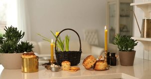 Easter preparation and holiday traditional decoration concept. Candles, easter pastry named kulich, eggs, green plants and basket with daffodils. 4K video
