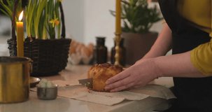 Woman cutting Easter cake into pieces and tasting it. Background candles at kitchen home with daffodils standing in the basket. High quality 4k video footage