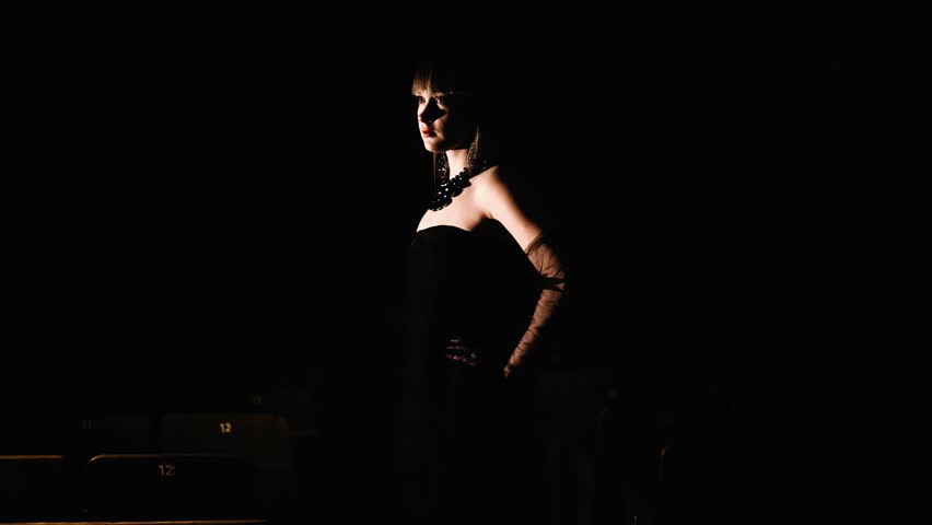 The girl walks through a dark room illuminated by a side light. Cool silhouette in motion